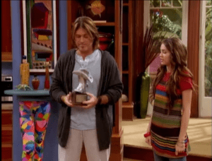 Robby looks down at his own Silver Boot award after telling Miley she's won one for best country/pop crossover