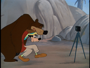 Goofy attempts to prop up the sleeping bear in the bear pit of the zoo for a photo op